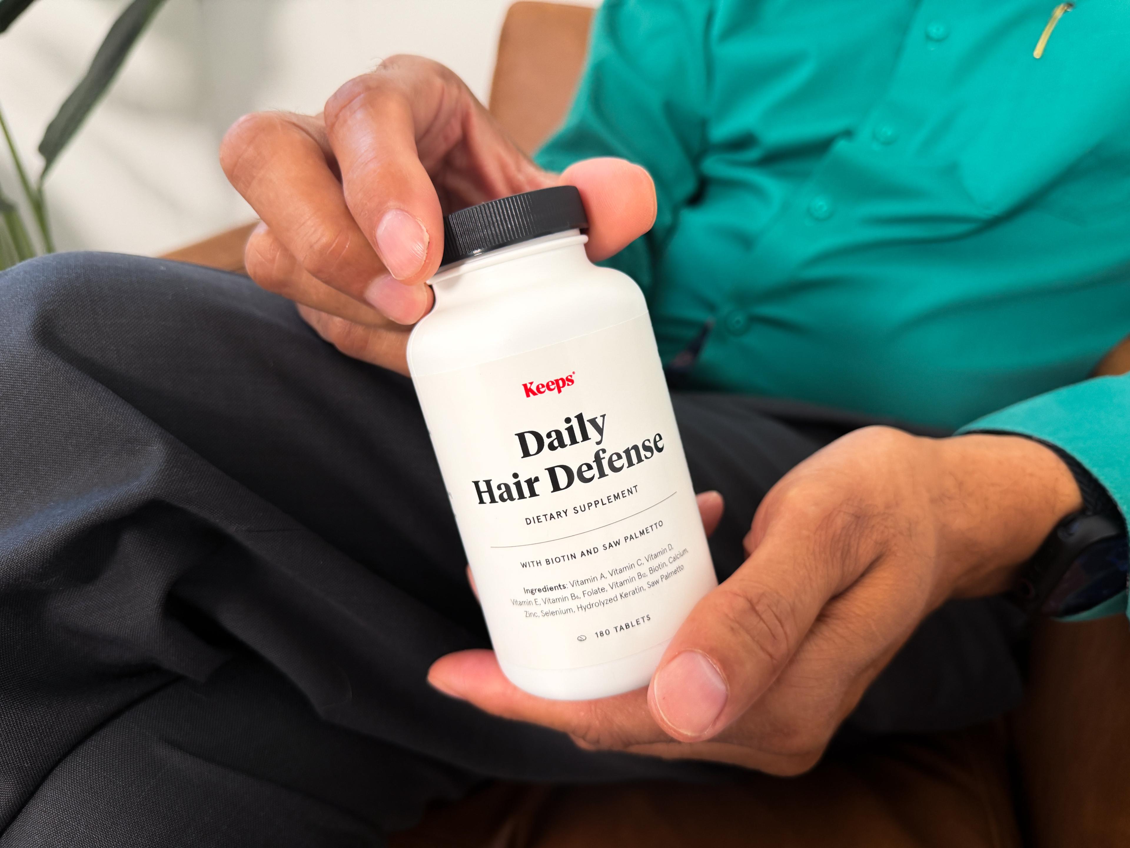 A man holding a white bottle of Keeps Daily Hair Defense Dietary Supplement