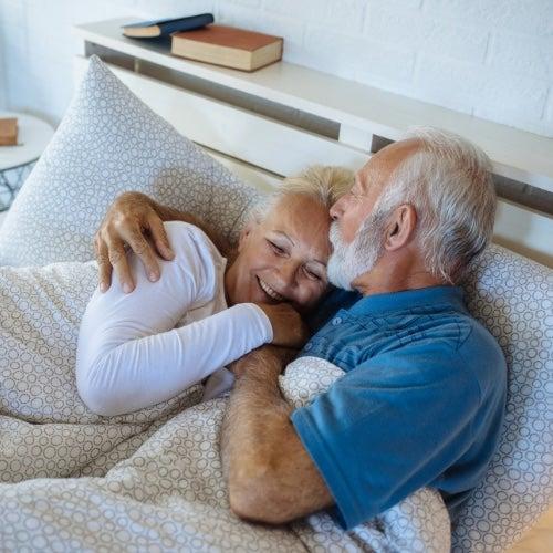 An older man and a woman cuddle together in a comfortable bed