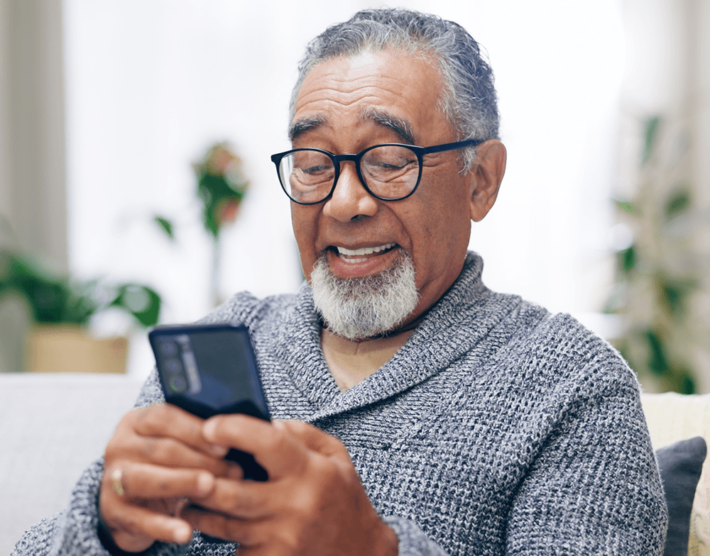 older man in black glasses smiling at cellphone
