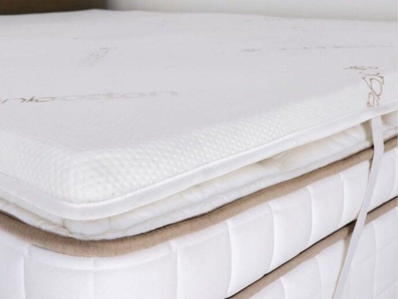 The Saatva Natural Latex mattress topper strapped to a bed