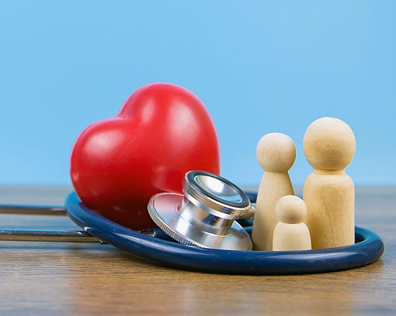 Red heart, wooden family figures, and a stethoscope on a blue background, symbolizing health and care.