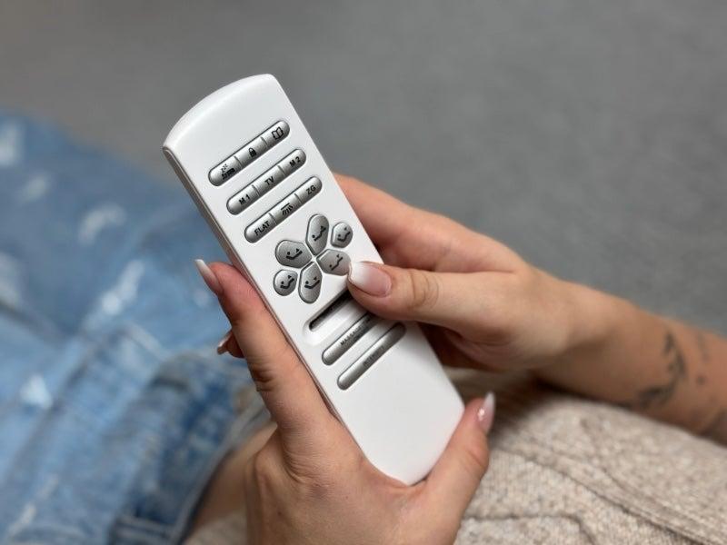 A woman's hand with long fingernails holds the remote to the Nectar adjustable base