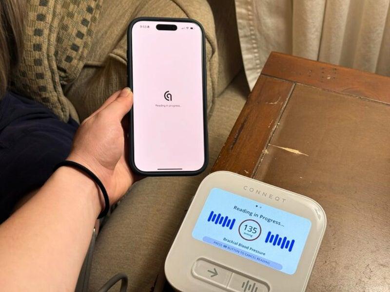 The Conneqt Pulse blood pressure monitor and a person holding a phone with the app on the screen