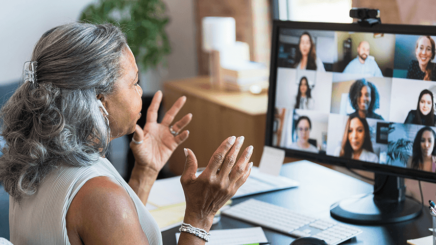 Black woman with gray hair gesturing at computer screen showing people in Zoom meeting