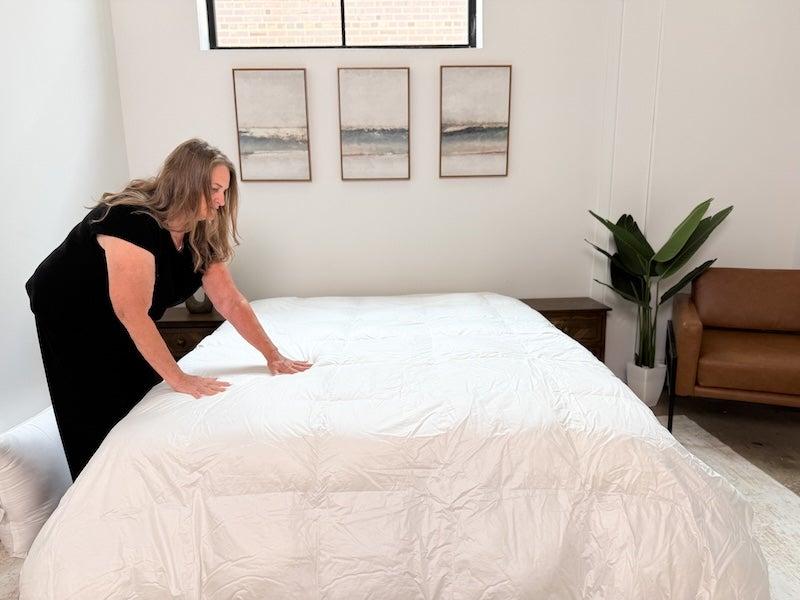 A tester leans over a bed and spreads her fingers out on the Saatva Down Alternative Comforter