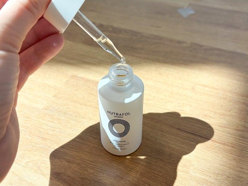 Fingers holding a white bottle with Nutrafol logo, with a dropper being lifted out of the bottle