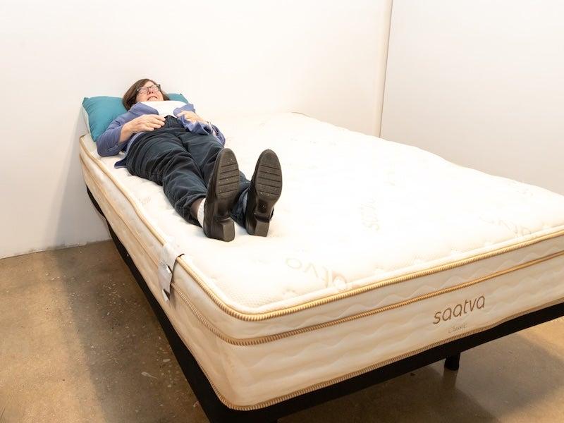 A woman in dark pants and a blue sweater lies on her back on the Saatva Classic Luxury Firm
