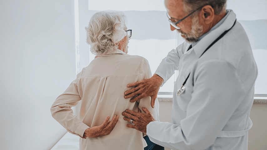 male doctor checking an older woman's back as she is faced away from him and touching her back