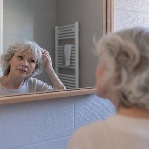 A woman stands in front of a bathroom mirror, fixing her hair