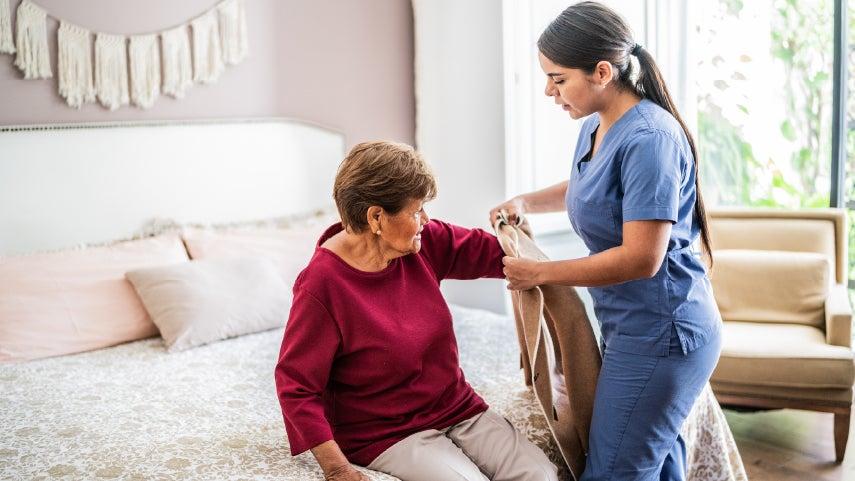Woman in scrubs helping another woman put her coat on.