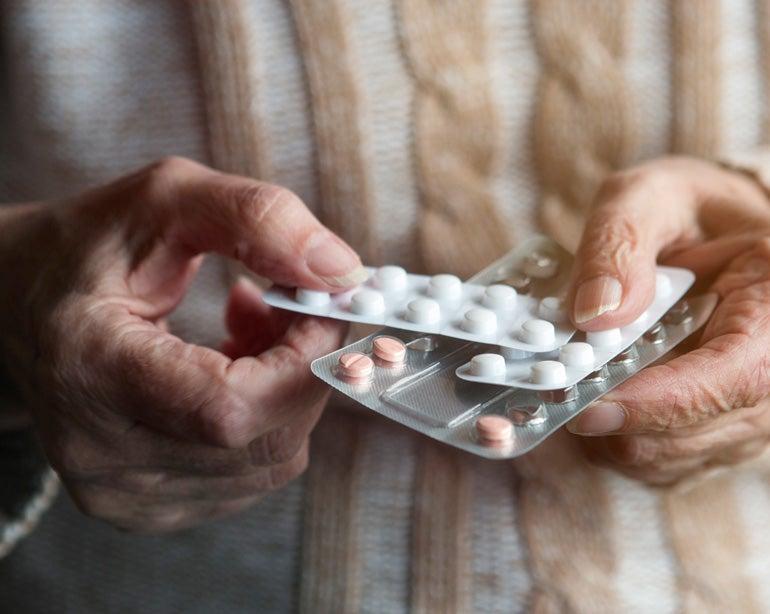 Close up shot of a senior woman holding a few packs of pills in her hands.