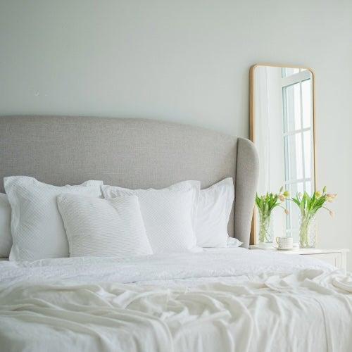 Sunlight filters into a room with a fluffy bed with white sheets