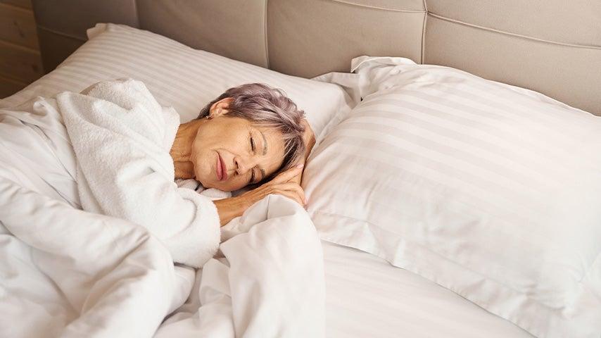 Older woman with short gray hair sleeping in bed with white sheets and pillowcases