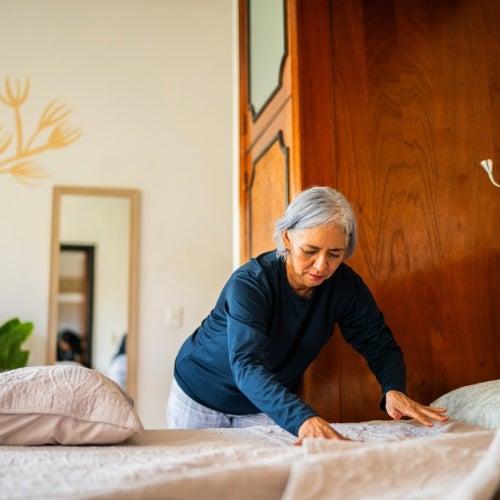 A woman with short white hair and a navy shirt makes a bed
