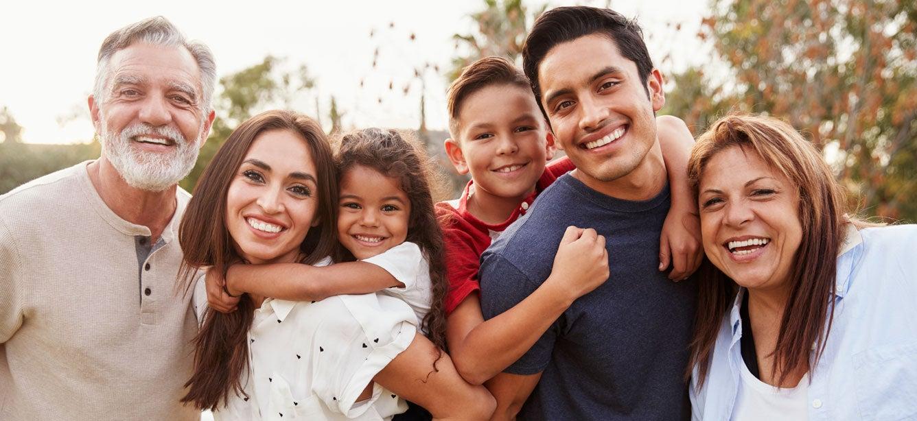 A happy multi-generational family smiles together outdoors, showcasing a grandfather, parents, and two children.