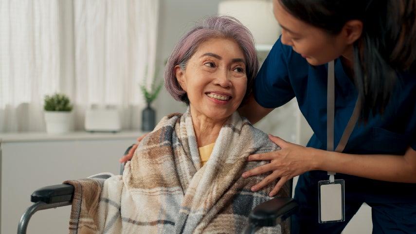 An Asian caregiver is helping, caring for a senior Asian woman in a wheelchair.