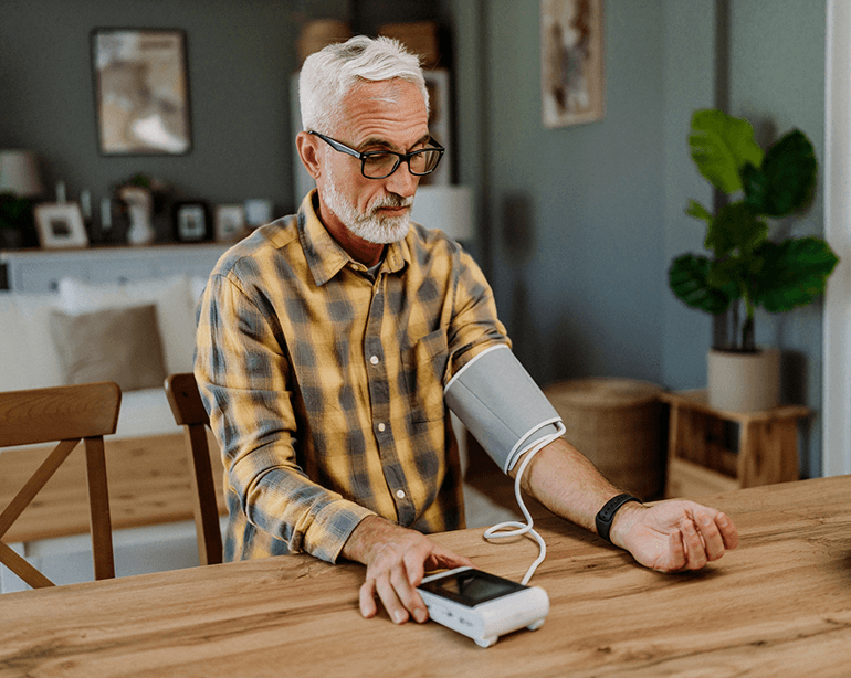 older man in plaid shirt sitting at table checking blood pressure at home