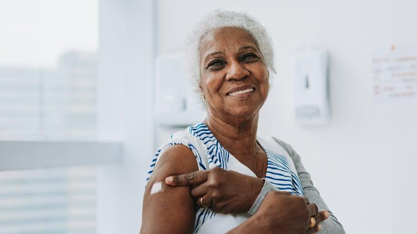 Woman smiles and points to band-aid on arm.
