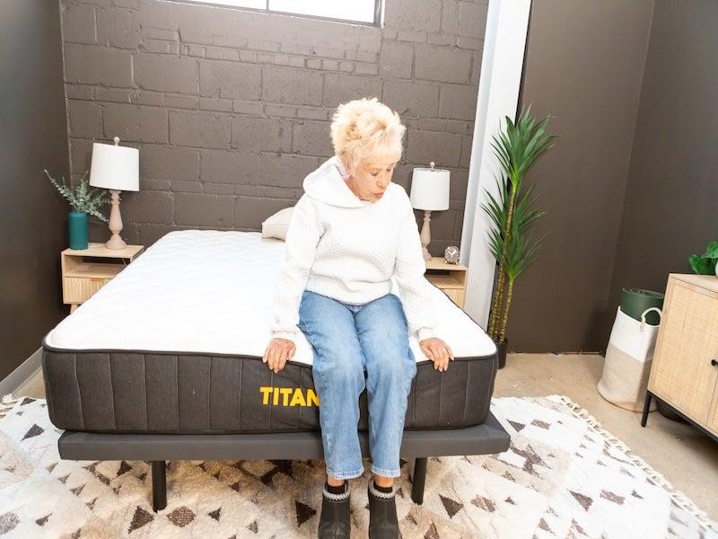 A woman sits on the edge of the Titan Plus Core mattress.
