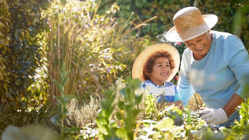 smiling grandson and grandmother wearing straw hats and working in garden