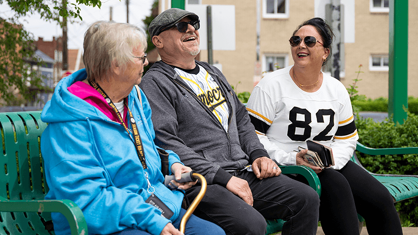three older adults laughing on a park bench