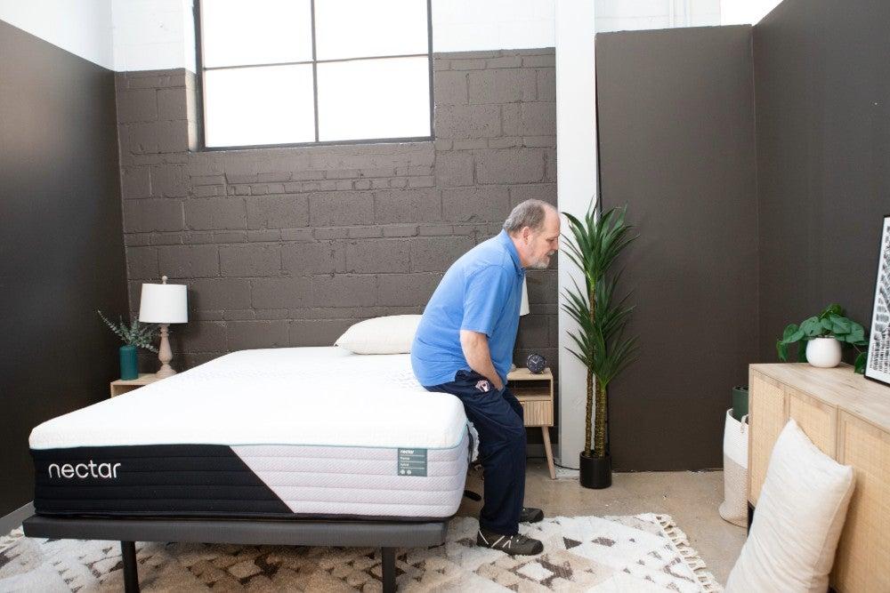 A man sitting on the edge of the Nectar Premier Hybrid mattress