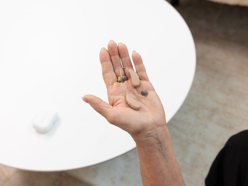 A person holding a pair of Audien ION Pro 2 hearing aids in the palm of their hand