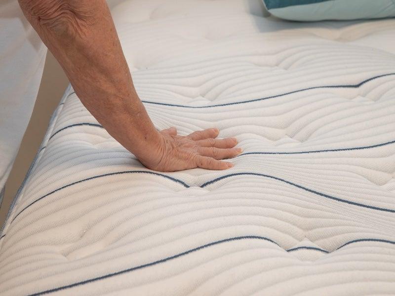 A hand presses down on the Bear Elite Hybrid mattress
