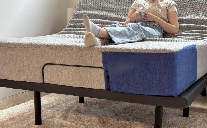 A woman sitting on a DreamCloud Adjustable Bed Frame in an upright position