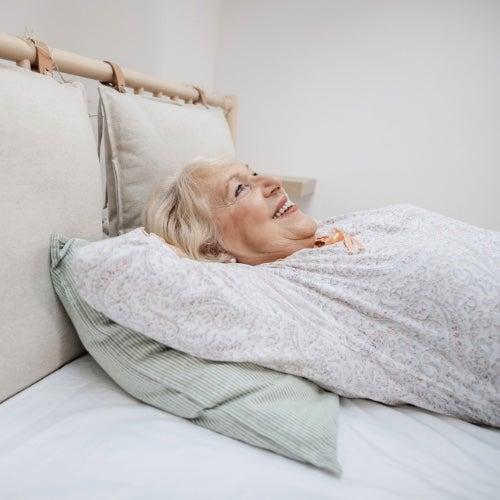A woman with white hair in a grey shirt lies back on a grey bed and smiles