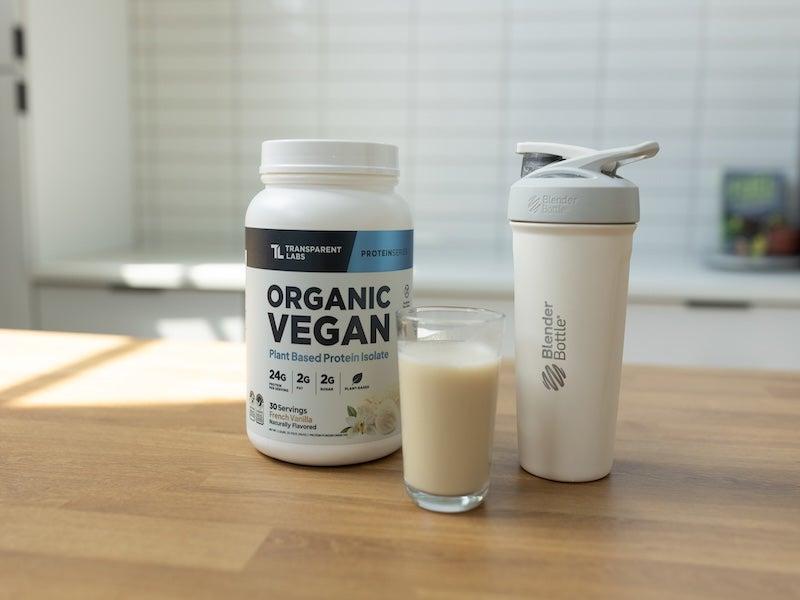Transparent Labs Vegan Protein Powder container next to a glass of it mixed with water