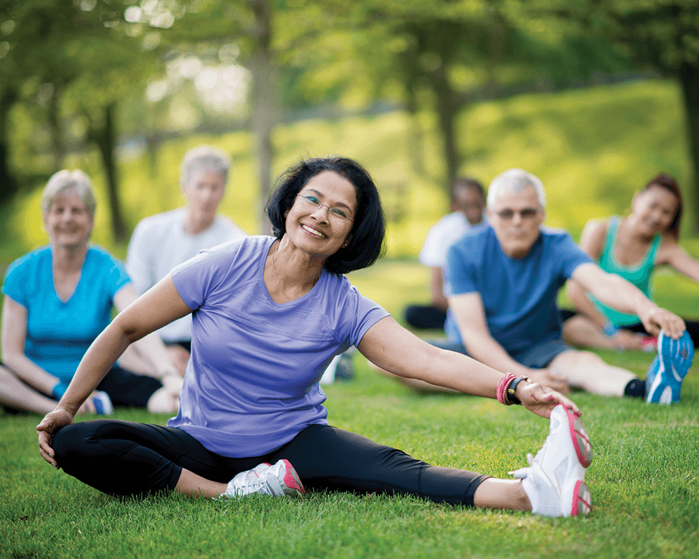 smiling older adults stretching on ground in an outdoor park
