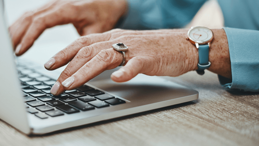 An older woman types at a laptop