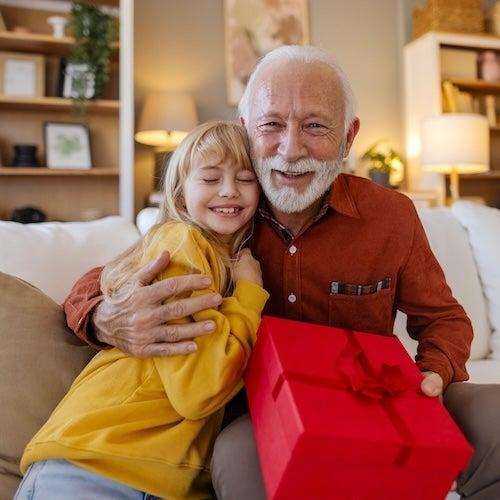 An older man hugs a young girl while holding a gift