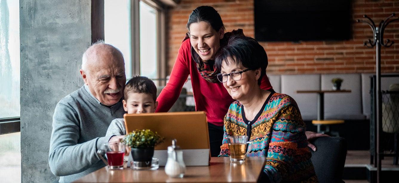 Smiling family gathered around a tablet, including two older adults, a young boy, and a woman