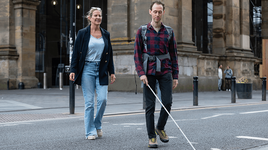 woman and man with white can crossing the street in front of a large historic building