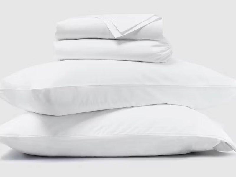A set of white Saatva Essential Luxury sheets against a white background