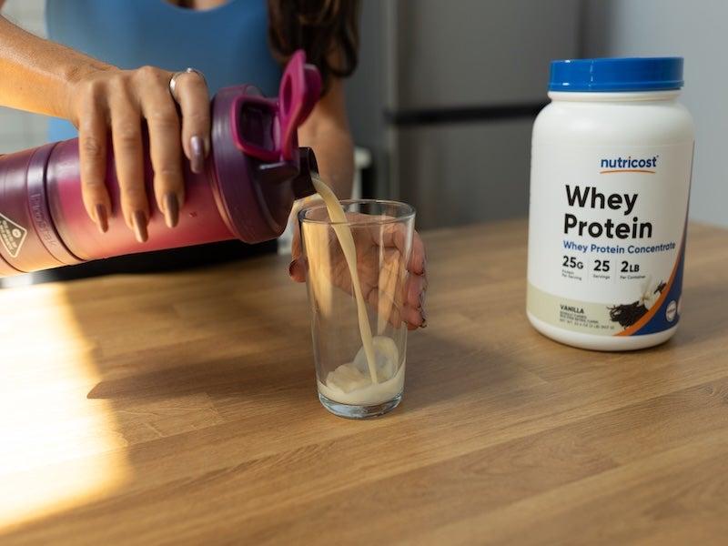 A woman pours Nutricost Whey Protein Concentrate drink into a glass