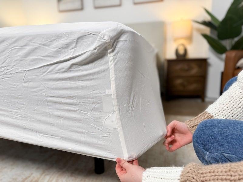 Two hands pull the fitted sheet from the Saatva Essential Luxury Sheet Set down over the mattress to show how it fits