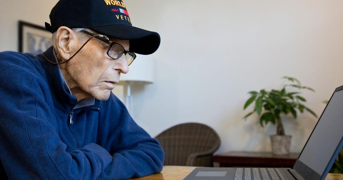 A retired Veteran is looking intensely at his laptop computer at his kitchen table.