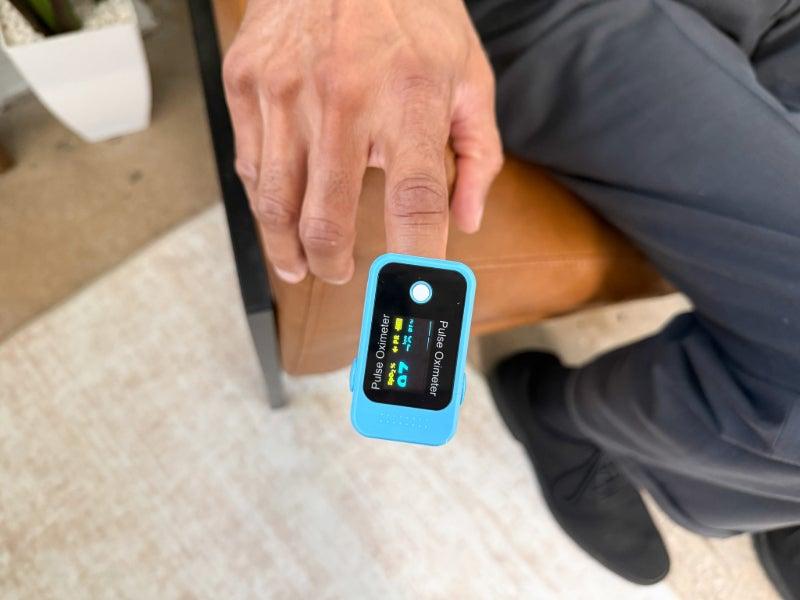 A person sitting on a leather chair uses the Baseline Finger Pulse Oximeter on their index finger