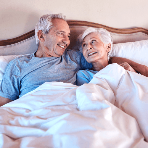 A man and a woman lying in bed together, smiling