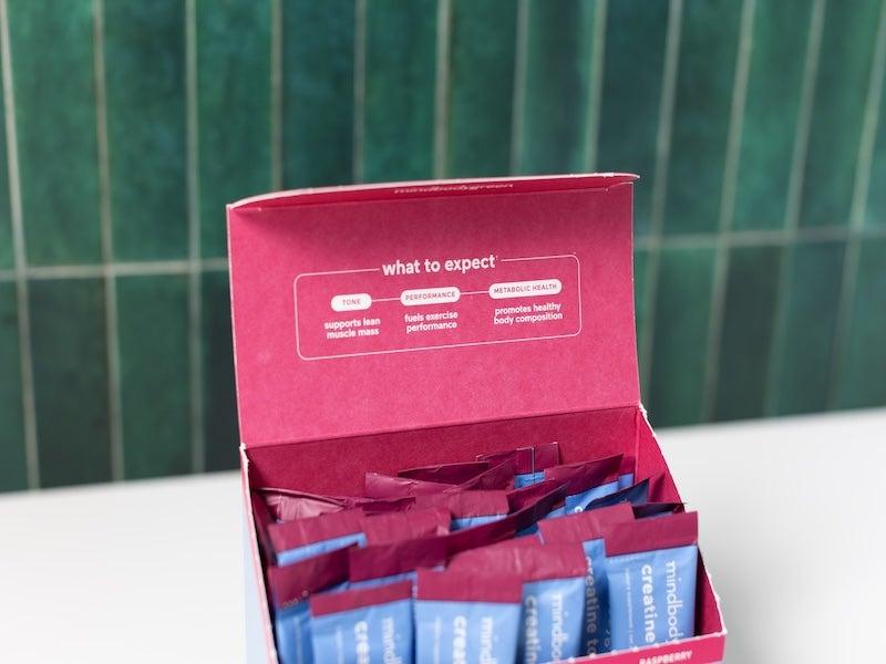 Blue and magenta box of Mindbodygreen Creatine Tone+ packets with the lid open