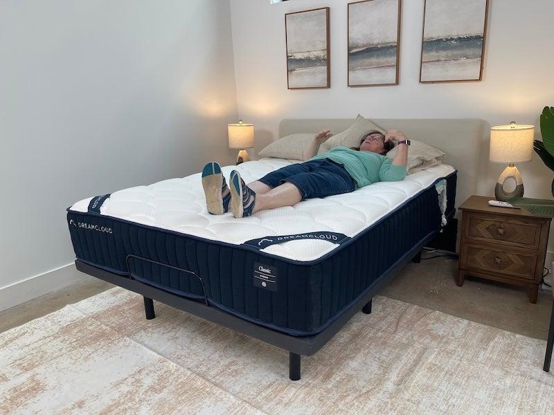 A woman in a teal shirt lies on her back on the DreamCloud Classic Hybrid mattress without sheets