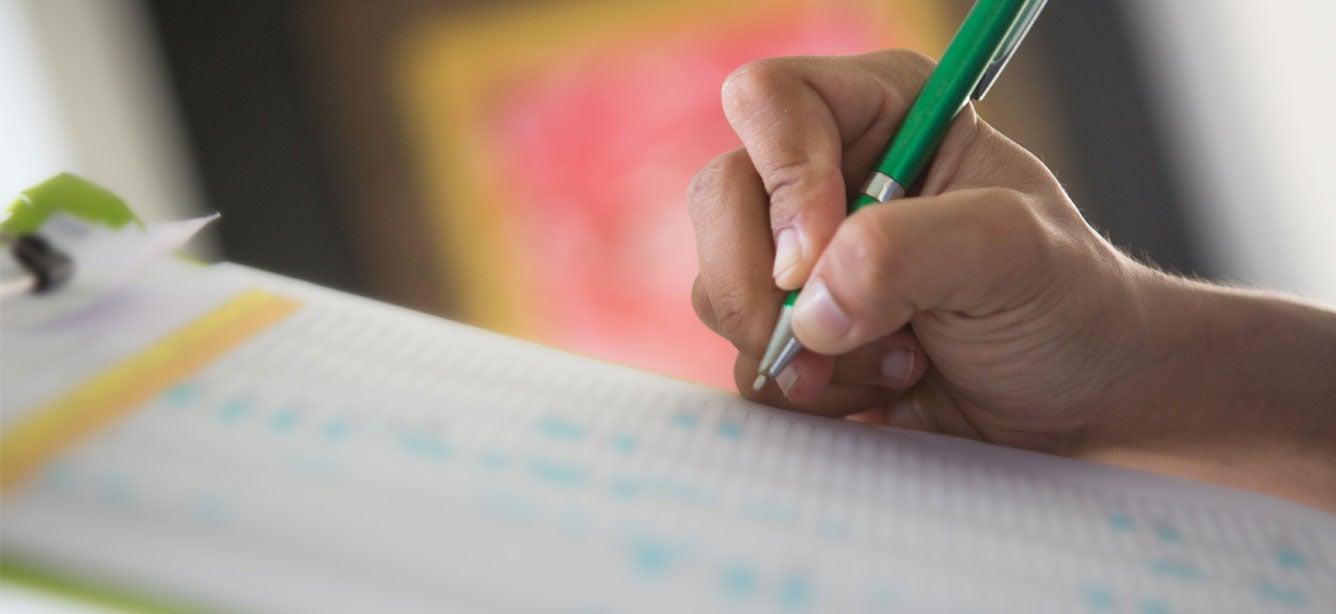 A woman is holding a checklist and marking things off with her green ballpoint pen.