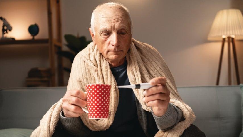 An older man 65+ is wrapped up in a blanket taking his temperature, worried he has RSV.