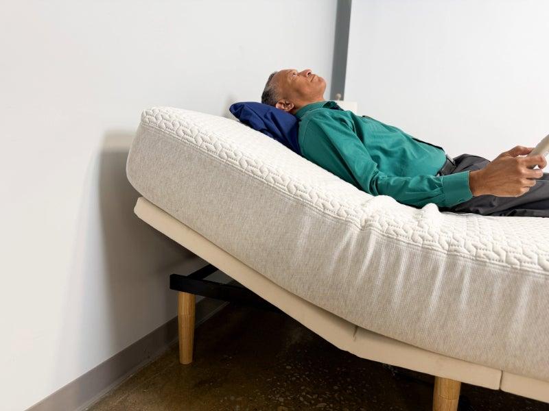A man lying on his back on the Silk & Snow Enhanced Adjustable Base with its remote in his hand