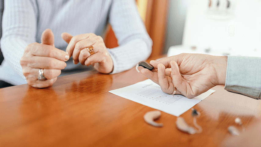 woman's hands across from a man's hand holding a hearing aid