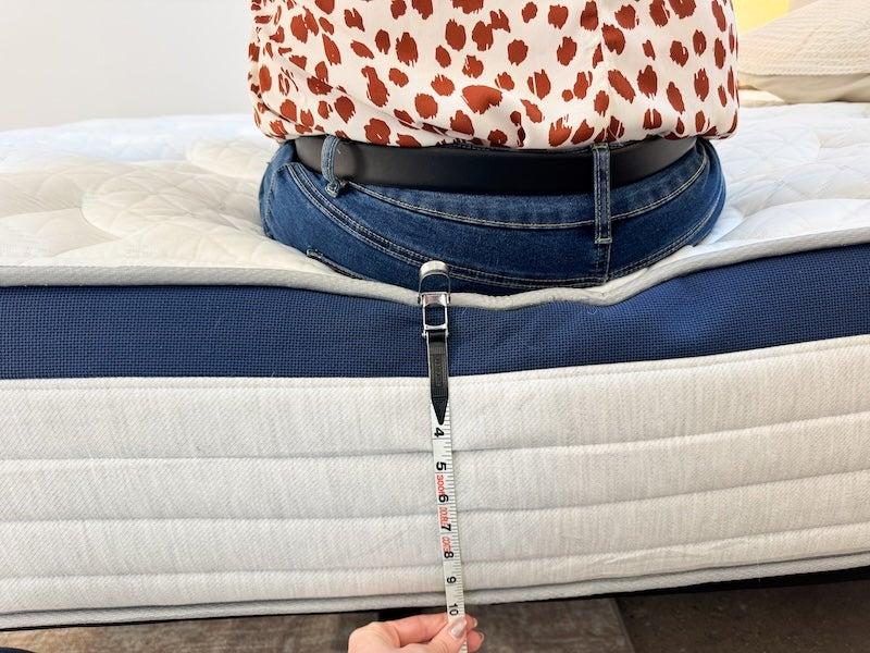 A woman sits on the edge of the Helix Midnight mattress.