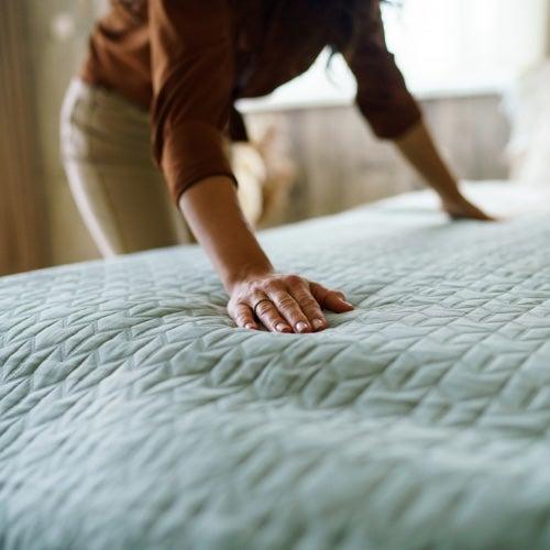 A woman spreads her hands over a made bed